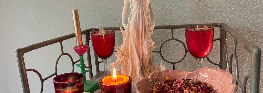 Photo of an altar with a statue of Aphrodite, surrounded by candles and with a bowl of rose petals